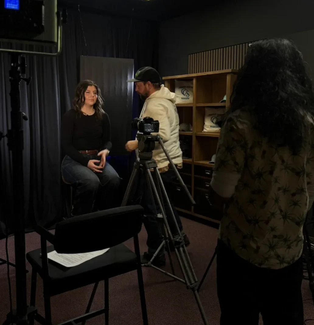 A recording session in progress at AV-Ator Studios: a seated guest on a lit set, a camera operator at the tripod, and a crew member running the shot.